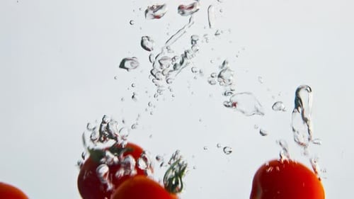 Tomatoes falling into clear water with bubbles