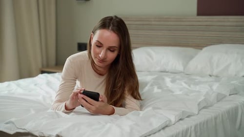 Woman Lying on Bed Using Smartphone at Home