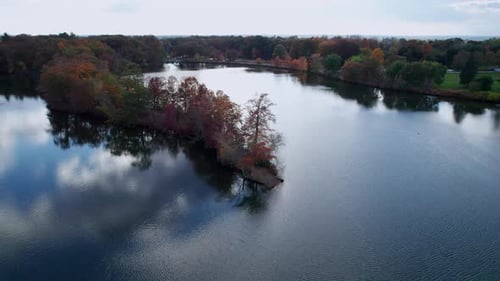 Aerial of a peninsula in a lake at Roger Williams Park full of trees in autumn colors.