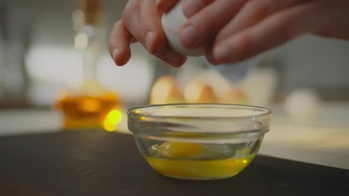 Die Hände des Kochs zerbrechen ein Ei und geben das Eigelb in eine Glasschüssel ab. Der Koch arbeitet mit Hühnchen