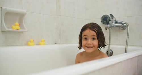 Happy Girl Splashing in Bathtub with Rubber Ducks
