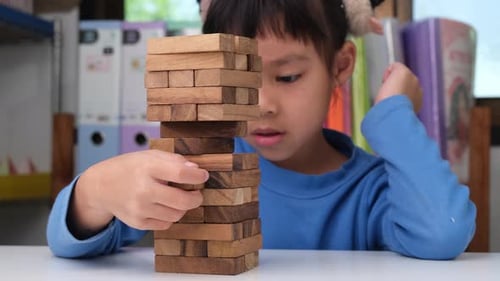 Süßes kleines Mädchen, das mit Holzspiel (Jenga) auf einem Tisch in einem Zimmer zu Hause spielt.