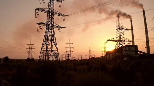 Electric towers near factory chimney with dark smoke.