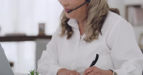 Ein erfahrener Call Center-Agent, der schreibt, während er ein Headset und einen Laptop benutzt, um zu helfen
