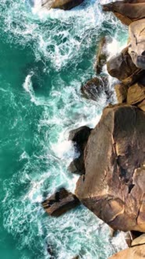 Glimpse of ocean waves crashing on rocky shore. Vertical video