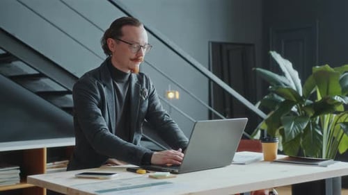 Focused Businessman Working on Laptop at Desk in Modern Office