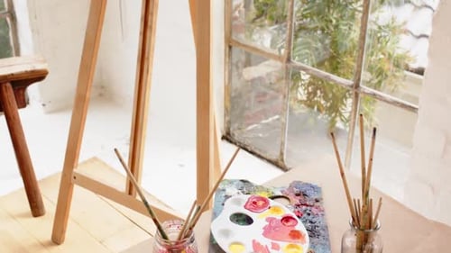 Easel with colorful abstract painting near window in cozy art studio, at home