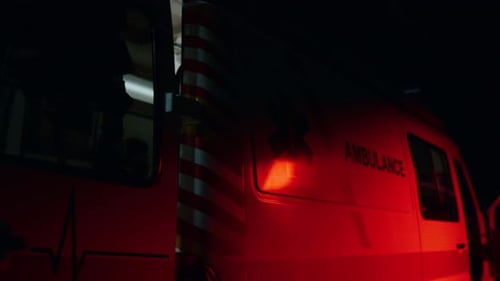 Emergency vehicle with medical logo lights flashing on city street at night