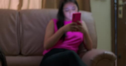 Junges Mädchen auf dem Boden, das in das Smartphone eingetaucht ist, zu einem älteren Mädchen auf der Couch, das sich auf das Gerät konzentriert,