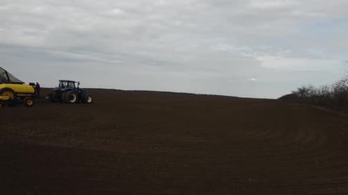 Blue tractor with yellow seeder working on the field in Ukraine OA