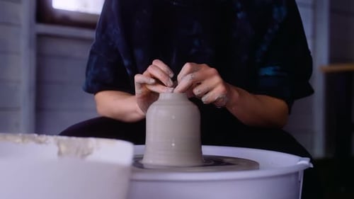 Potter puts finishing touches on clay vase on pottery wheel in her workshop closeup on clay vase