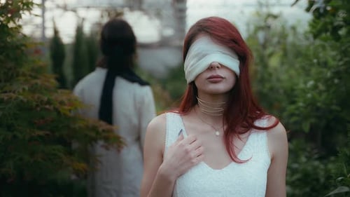 Zeitlupe eines jungen Paares mit verbundenen Augen, das sich im sonnenbeschienenen Gewächshaus gegenübersteht