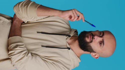 Man Ponders with Pen on Blue Background