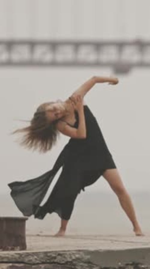 Woman in Black Dress Dancing on Concrete Pier