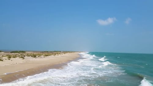 Aerial drone shot of ocean tides in the ocean beside a beach on a sunny day