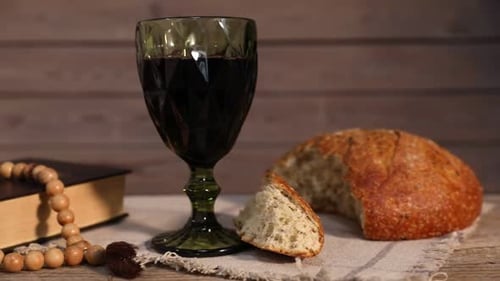 Sakrament der Kommunion. Glas Rotwein, Brot, Rosenkranz und Bibel auf dem Tisch vor einer Holzwand