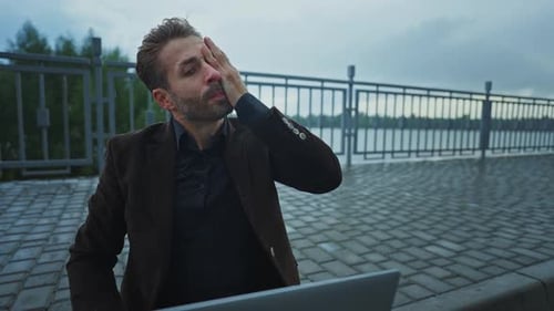 Man Sheltering From Rain with Laptop Outdoors