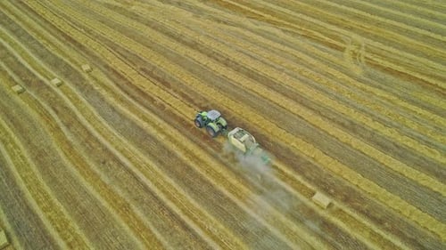 Hay Baler Tractor Driving Across the Field Collecting Straws and Making the Bales Aerial Scenery in