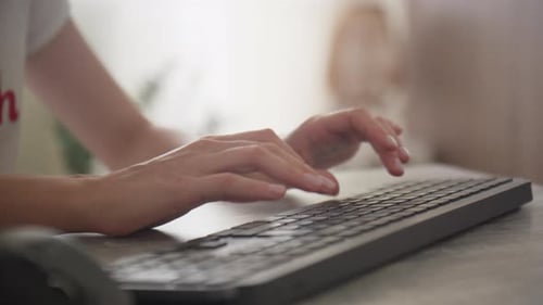 Woman Typing on Keyboard at Desk in Bright Room