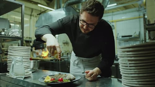 Chef Pouring Olive Oil over Seafood Dish on Plate in Restaurant Kitchen