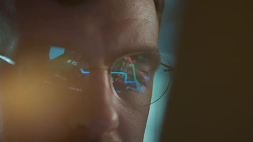 Trader Wearing Glasses is Working on Laptop Computer Screen with Stock Market Charts and Bitcoin BTC
