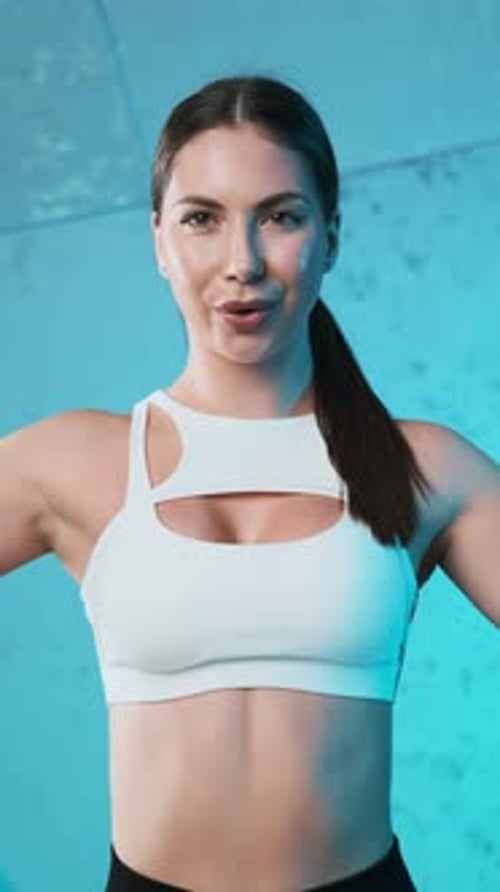 Portrait of energetic young fitness girl in white top and black shorts doing warm-up, breathing deep