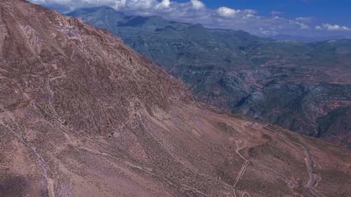 Low-angle aerial flight following the contour of a steep mountain ridge overlooking a deep valley