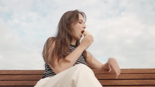 Woman Sits on Bench Eating Ice Cream