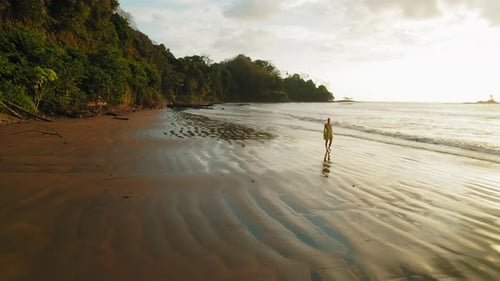 Young woman walks on wet sand at Dominicalito Beach during sunset Costa Rica