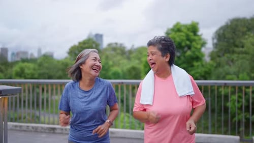 Two happy Asian senior women jogging exercise outdoors in modern city.