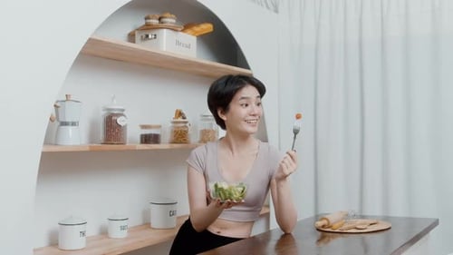 An Asian young woman in sportswear eating vegetables salad