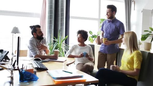 Happy creative team drinking coffee and talking at break in modern office