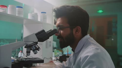 Face of Young Man Scientist with Glasses and Protective Gloves Looking Under the Microscope Turn