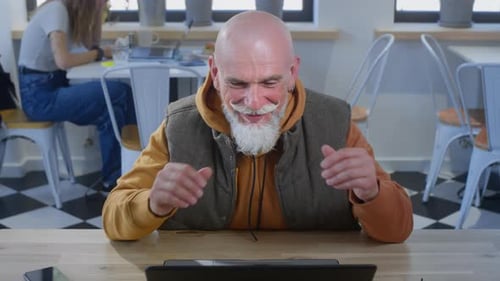 Stylish Old Man Conducts a Video Call in a Cafe or Restaurant with a Laptop Grandfather is a