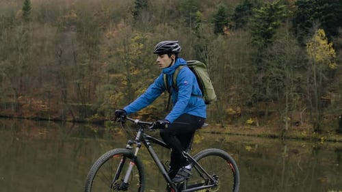 Young man cycling through autumn forest nature with reflection on lake