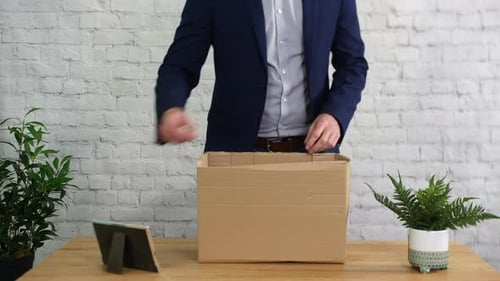 A man fired from work is packing a box on his desk and leaving his job as unemployed