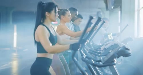 A Diverse Group of Individuals Engaged in a Rigorous Workout Routine on Elliptical Machines at a Gym