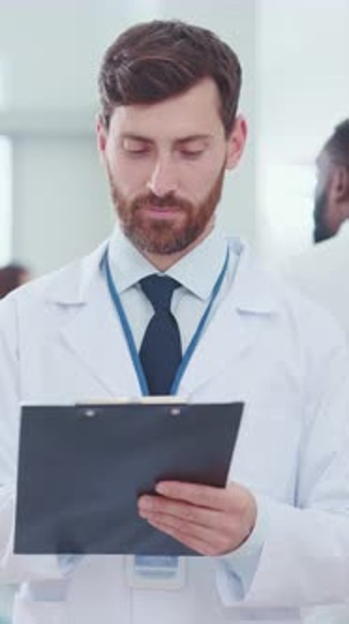 Male Doctor Smiling, Holding Clipboard in Hospital
