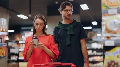 Handsome Young Couple Standing in Supermarket Section Reading Nutrition Information on Foods