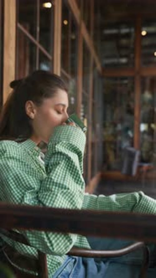 On the Cafe's Summer Terrace a Lovely Young Woman is Drinking Coffee and Holding a Smartphone