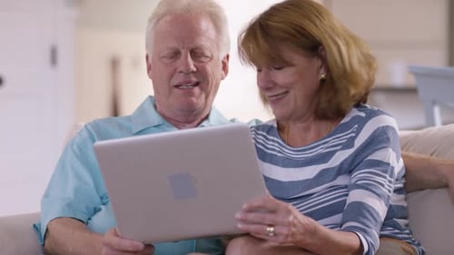 Senior couple smiles using laptop together on sofa