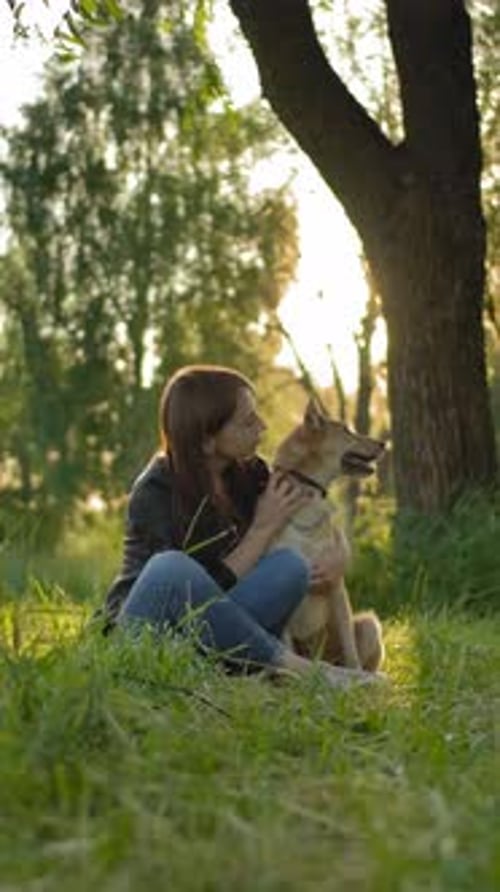Young Woman Hugging Dog at Sunset in Park