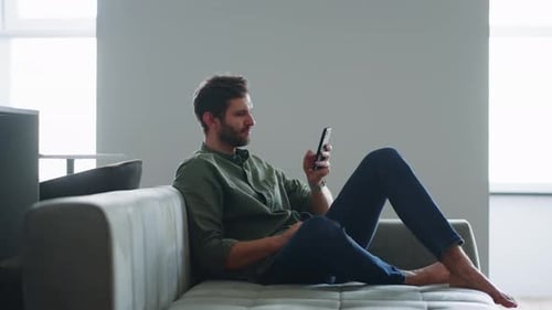 Man Lounging on Couch Uses Smartphone