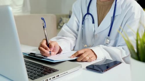 Doctor or Nurse in Uniform with Stethoscope Writing Something Information of Patient in Paperwork