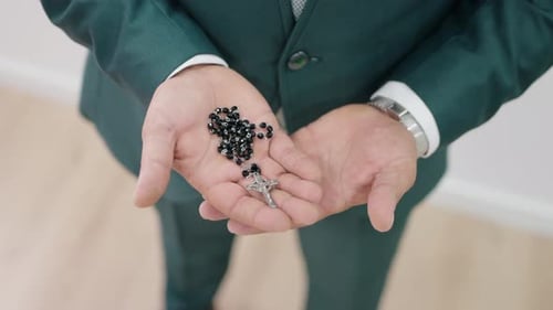 Man Holds Rosary Beads and Cross in Hands