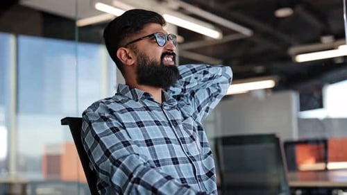 Tired Bearded Businessman Massaging Neck While Sitting in Modern Office
