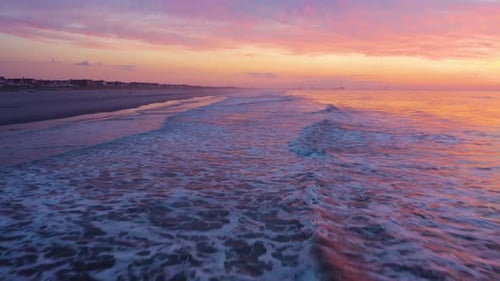 Aerial, waves break onto sandy beach, spectacular purple and orange sunset