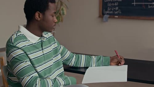 Portrait d'un étudiant noir de sexe masculin écrivant des notes en classe