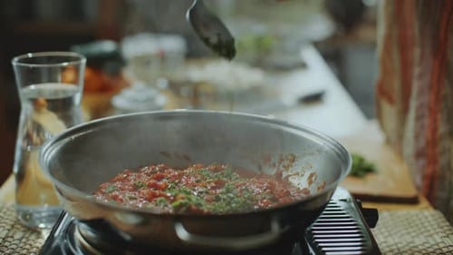 Close-Up of Adding Fresh Herbs to Simmering Tomato Sauce in Pan