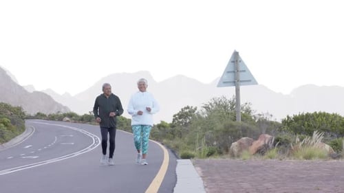 Happy senior biracial couple running on road in mountains